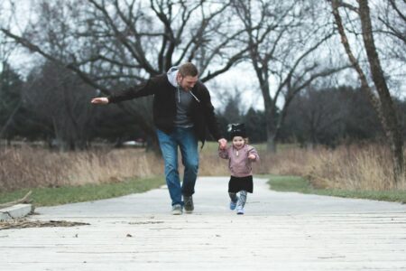 a father and his little girl running on a park pathway